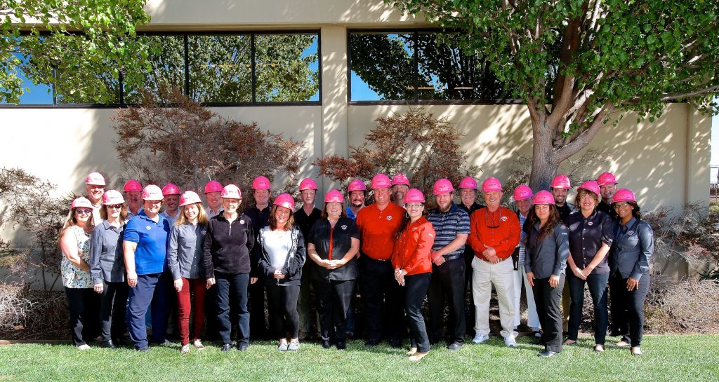 PMI construction workers proudly pose wearing their EMCOR/ PMI Pink Hard Hats.
